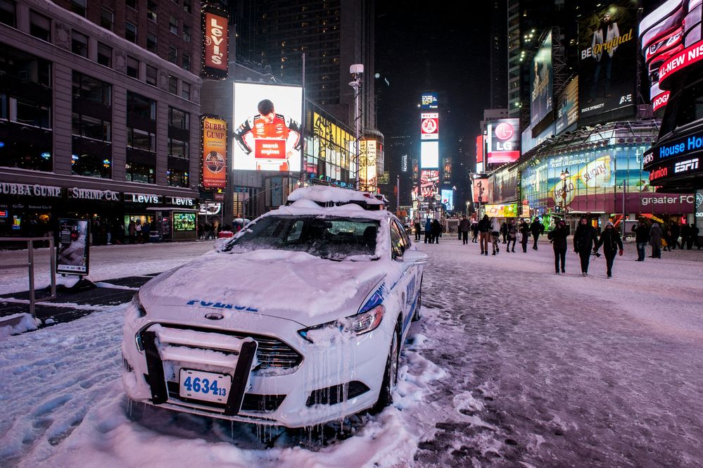 Times Square nachts im Tiefschnee, im Vordergrund ein vollständig eingeschneiter Streifenwagen, dahinter die Leuchtreklamen